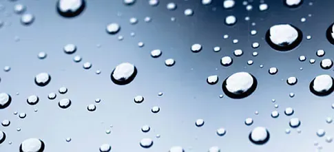 Gotas de agua sobre una superficie lisa y reflectante. El fondo pasa de azul claro a azul oscuro.