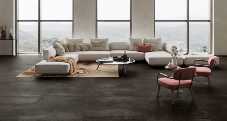 Amplia sala de estar con un sofá seccional color crema, dos sillas rosas y una ventana con vista a un paisaje.