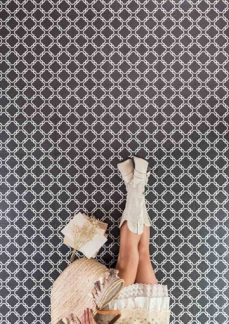 Las piernas de una mujer con botas blancas descansan contra una pared con un estampado oscuro, con una caja de regalo y un chal mullido.