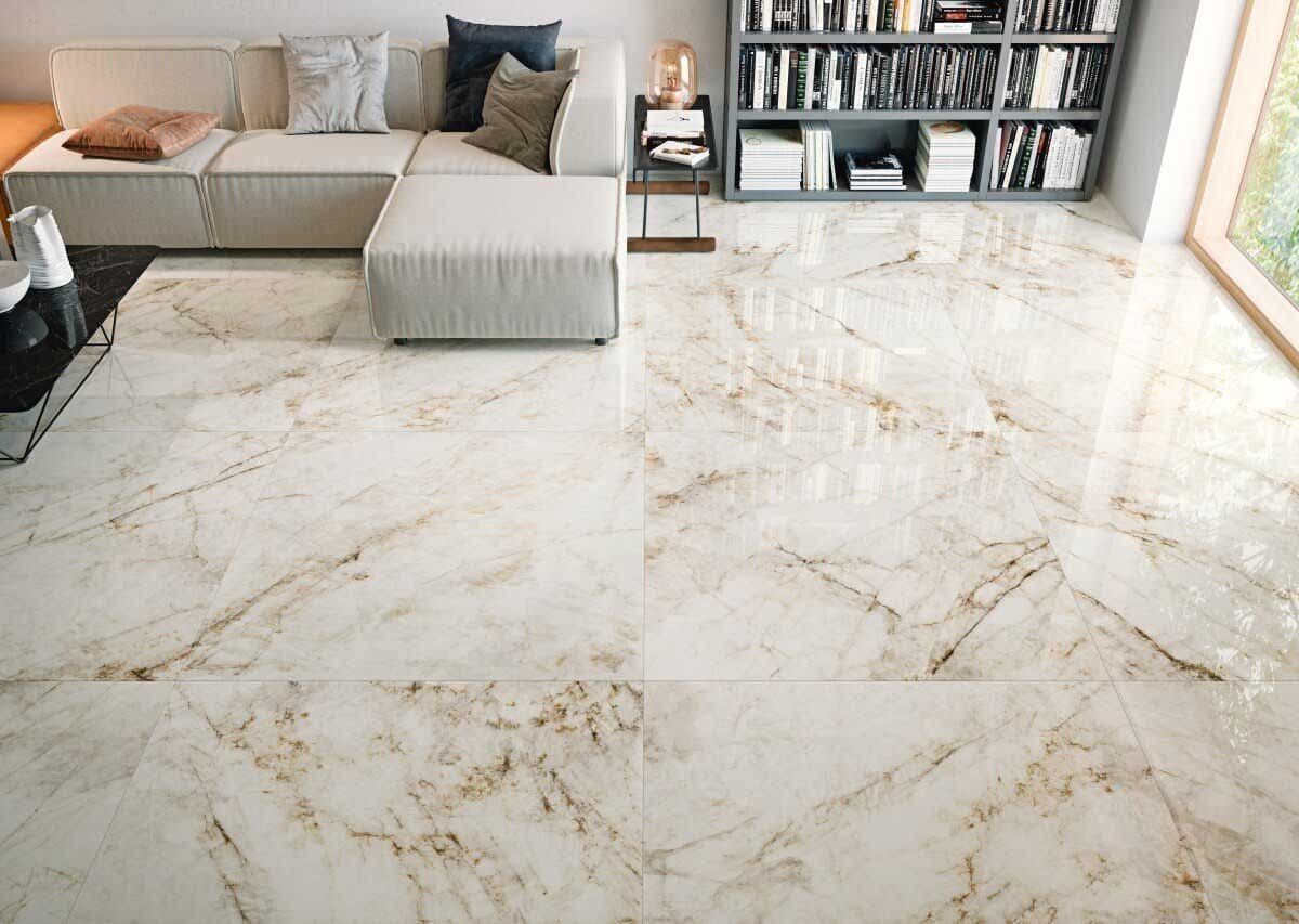 Sala de estar con piso de mármol beige, sofá seccional color crema y estantería.