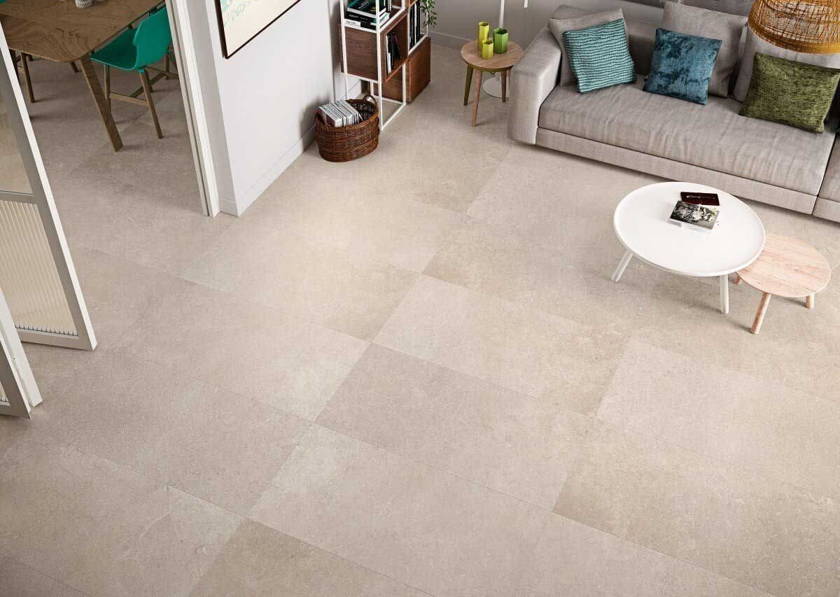 Sala de estar con piso de baldosas de color claro, sofá beige, mesa de café redonda y puerta abierta.