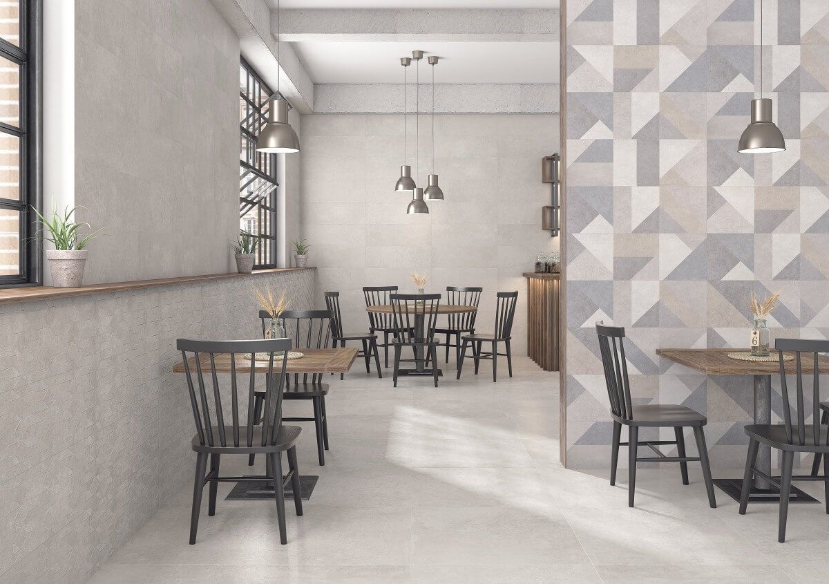 Interior de restaurante con mesas y sillas, pared geométrica decorativa y elementos de diseño industrial.