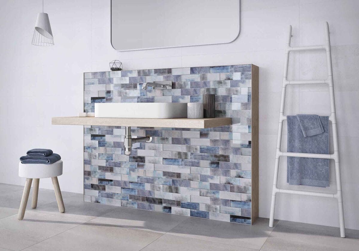 Baño moderno con mosaico azul, lavabo flotante, estante de madera y escalera con toallas.