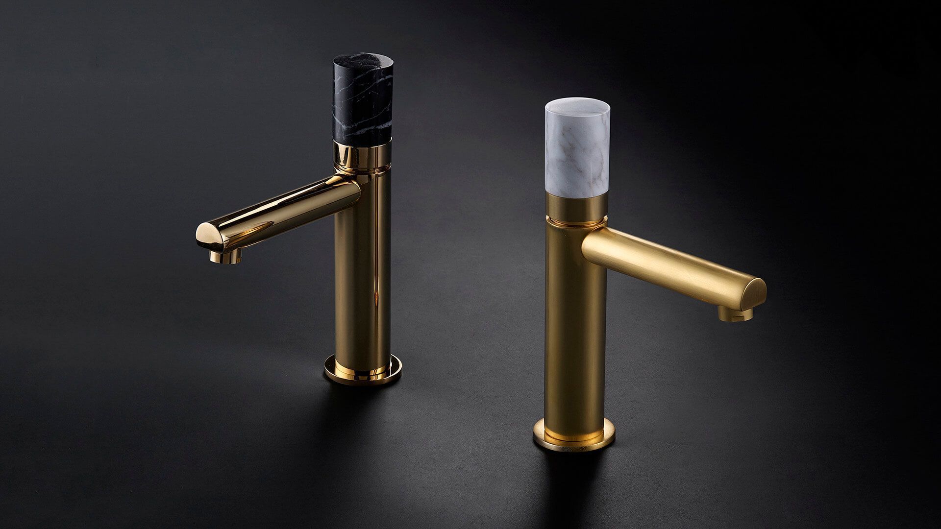 Dos grifos en tonos dorados con tapas con estampado de mármol, sobre un fondo oscuro.