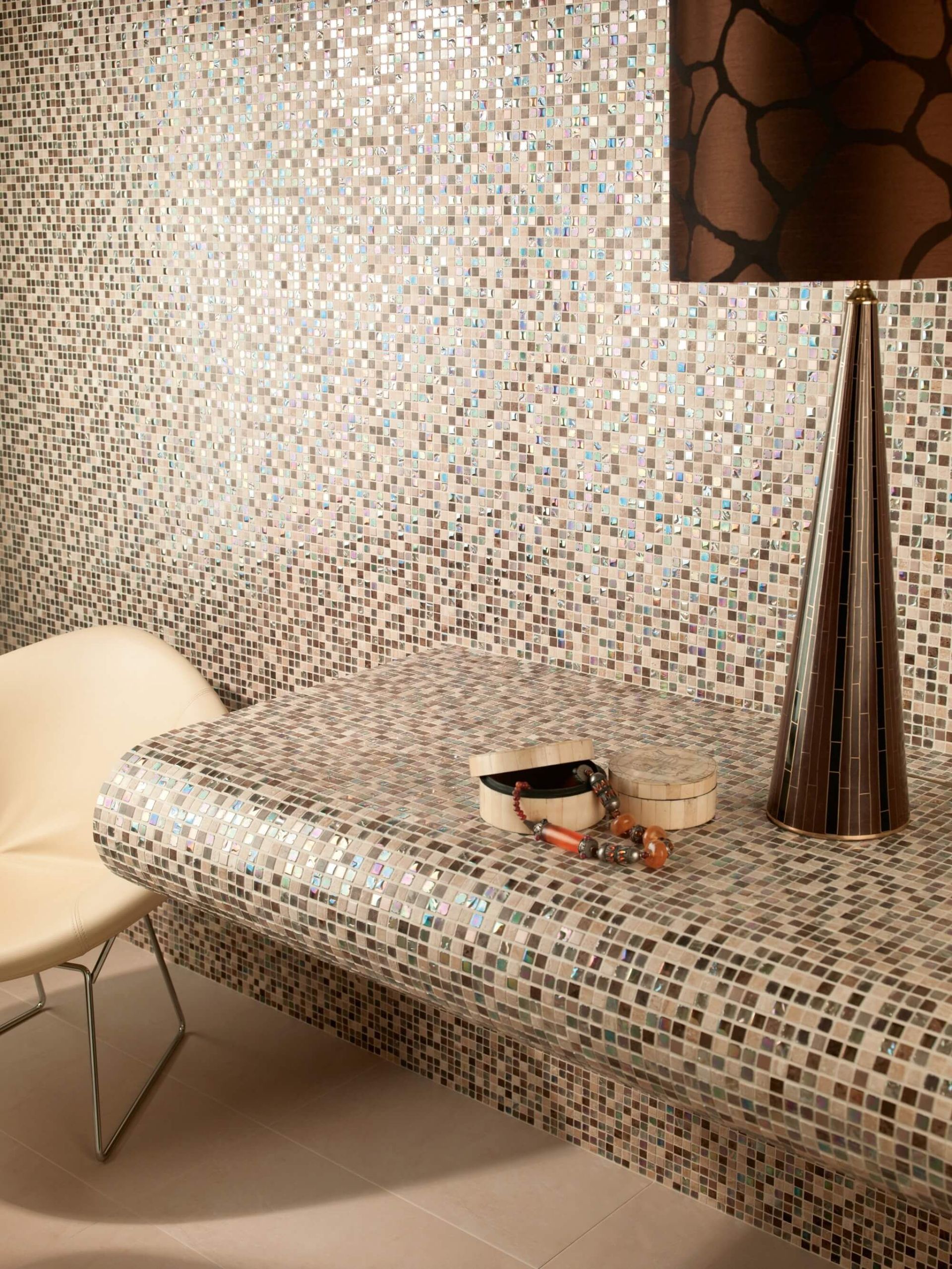 Mostrador y pared de mosaico, con lámpara y silla. Joyas sobre el mostrador.