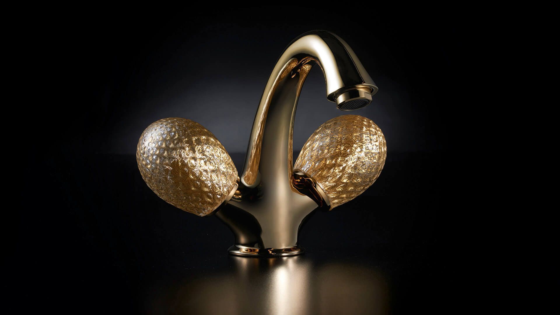 Grifo de color dorado con manijas texturizadas sobre un fondo oscuro, una gota de agua en el caño.