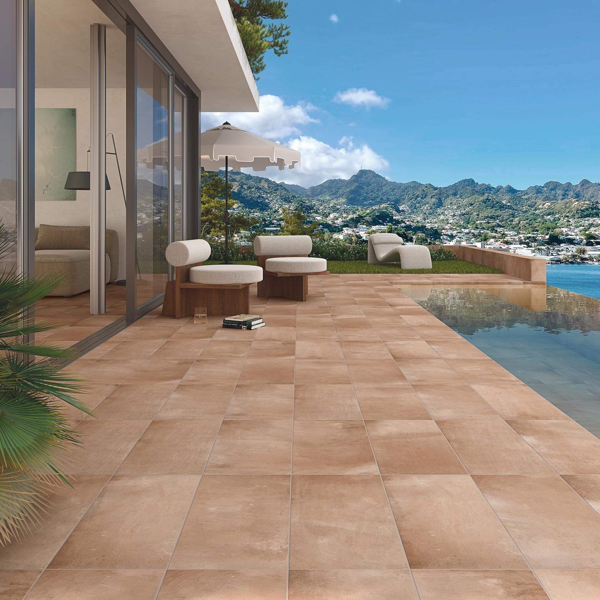 Terraza con azulejos marrones con vistas al agua y a las montañas, zona de estar con sombrilla.