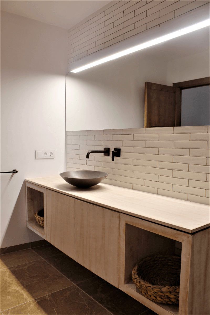 Baño moderno con tocador flotante de madera, lavabo sobre encimera, grifo negro y pared de azulejos.