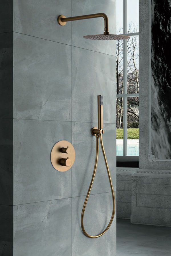 Accesorios de ducha dorados sobre pared de azulejos grises, incluido cabezal de ducha de lluvia y rociador de mano.