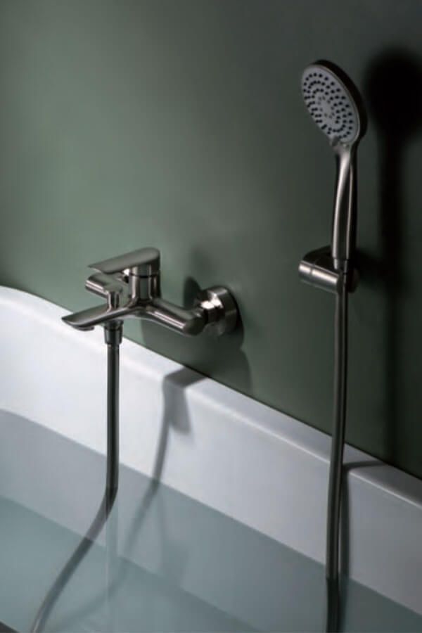 Bañera con grifo y ducha de mano contra una pared verde, llena de agua.