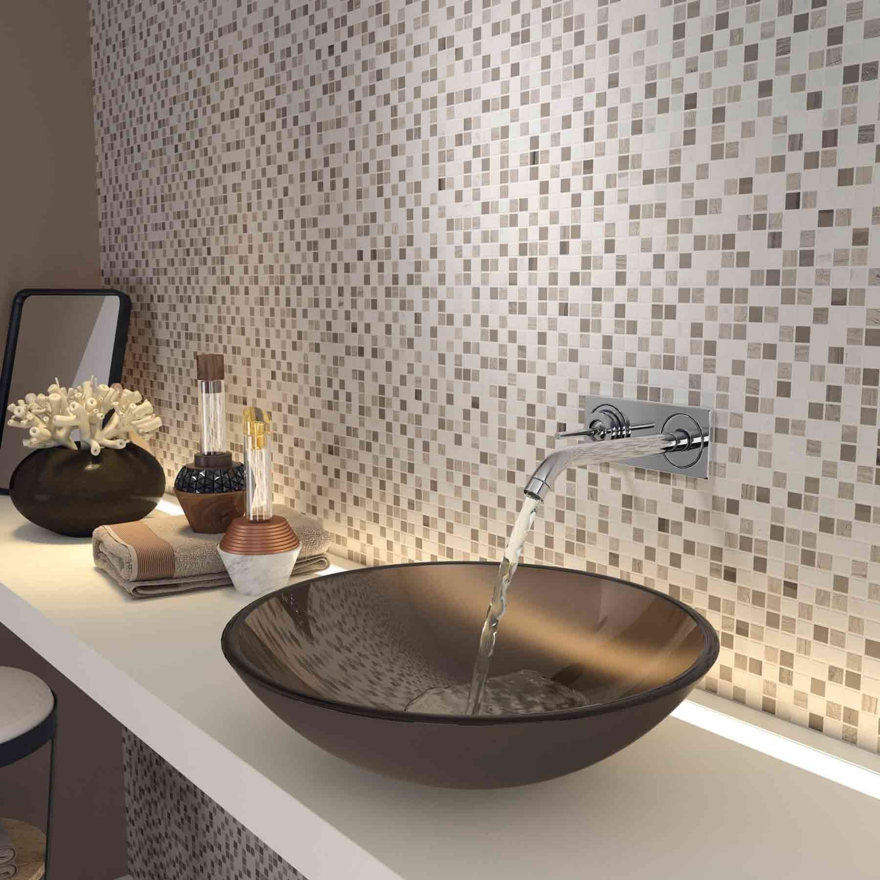 Baño con pared de mosaico, lavabo sobre encimera y grifo cromado. El agua fluye hacia una taza de vidrio marrón.