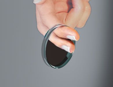 Mano sosteniendo una lente circular; la lente refleja una superficie oscura y sombreada.