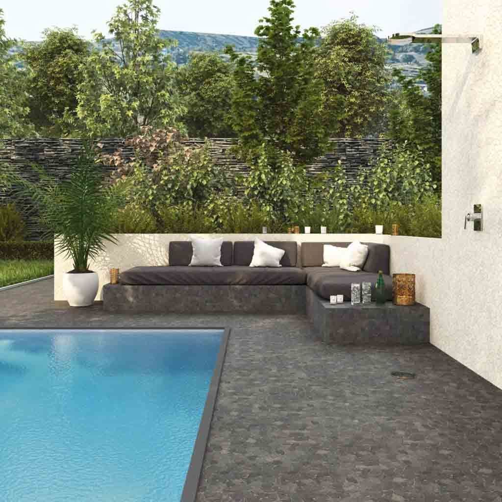 Área de descanso junto a la piscina con asientos de color gris oscuro, almohadas y exuberante vegetación de fondo.