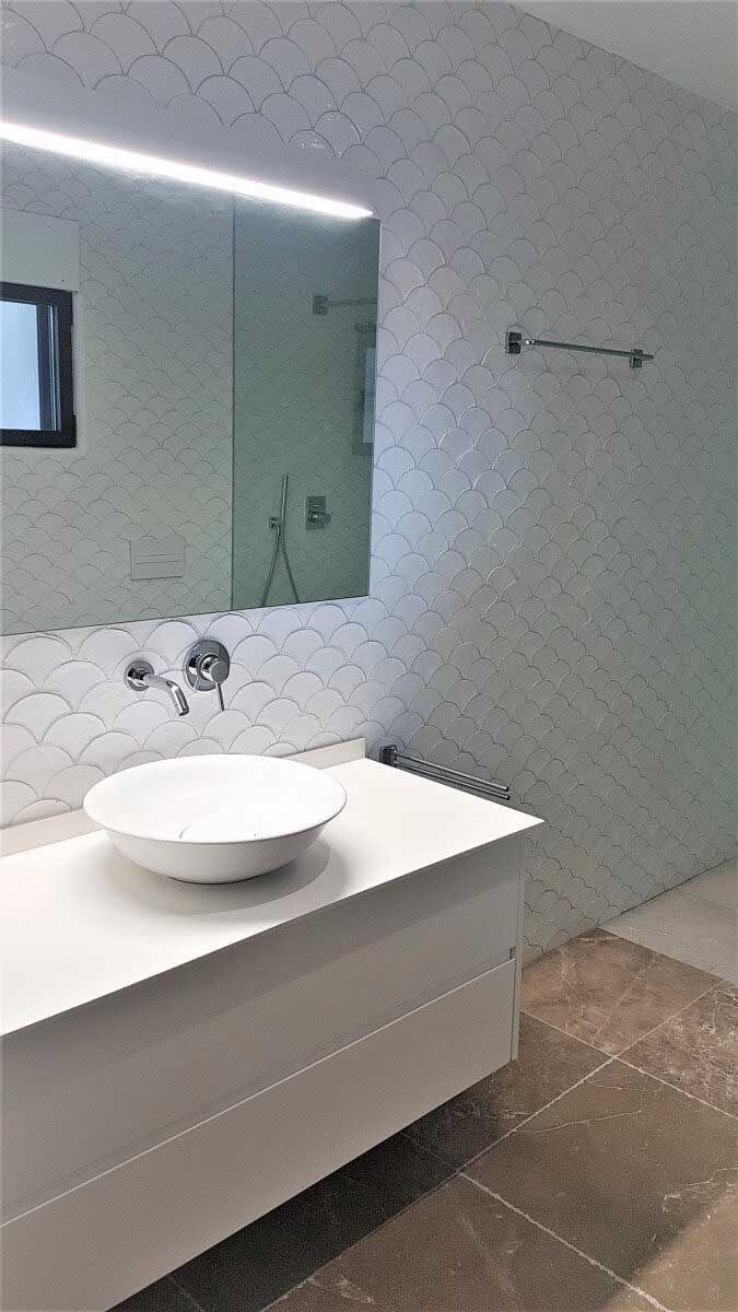 Baño blanco moderno con lavabo, espejo grande, pared texturizada y toallero.