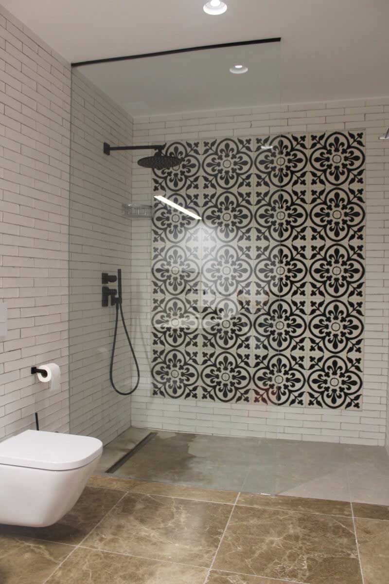 Baño moderno con ducha con azulejos estampados, puerta de cristal e inodoro montado en la pared.