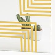 El diseño geométrico amarillo sobre una superficie transparente oscurece parcialmente los cactus en macetas.