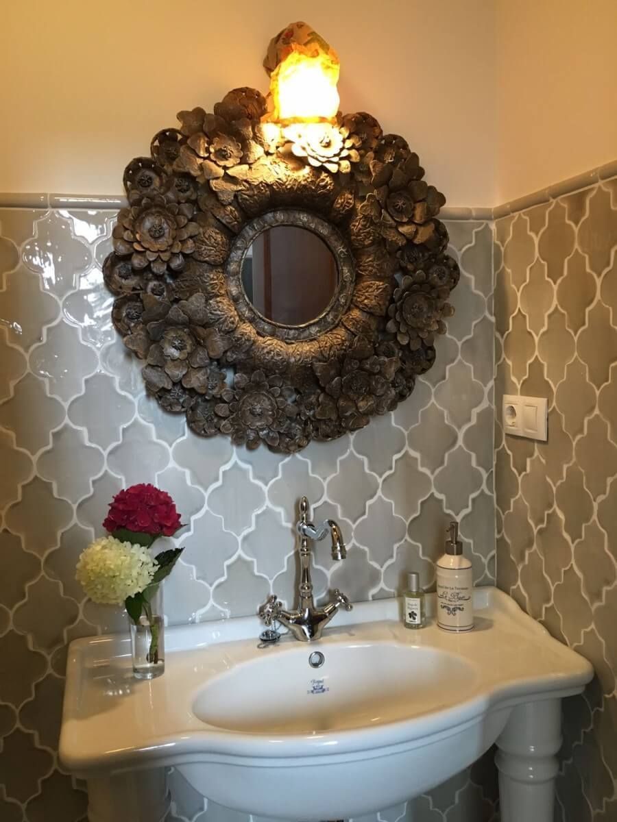 Lavabo de baño con espejo decorativo, flores y pared de azulejos estampados.