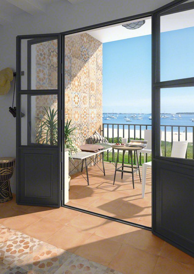 Las puertas del balcón se abren a la vista del mar, mesa y sillas en el patio, pared de azulejos estampados.