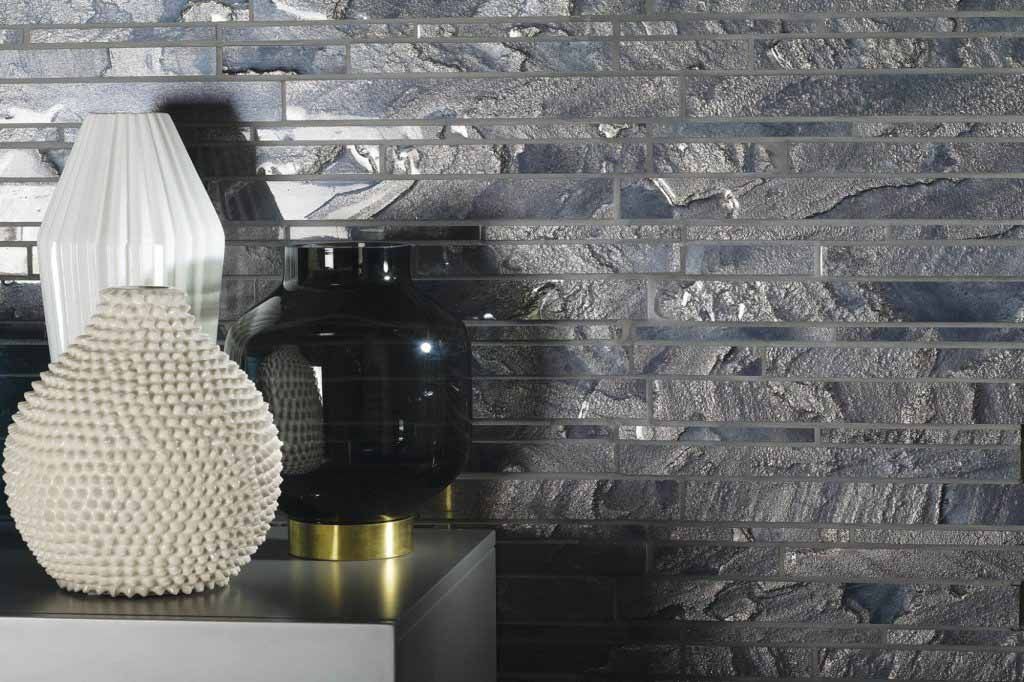 Estantería decorativa con tres jarrones frente a una pared de azulejos texturizados de color gris plateado.