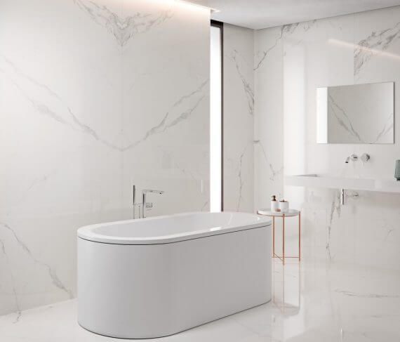 Baño blanco moderno con bañera independiente, lavabo y paredes y suelo de baldosas símil mármol.