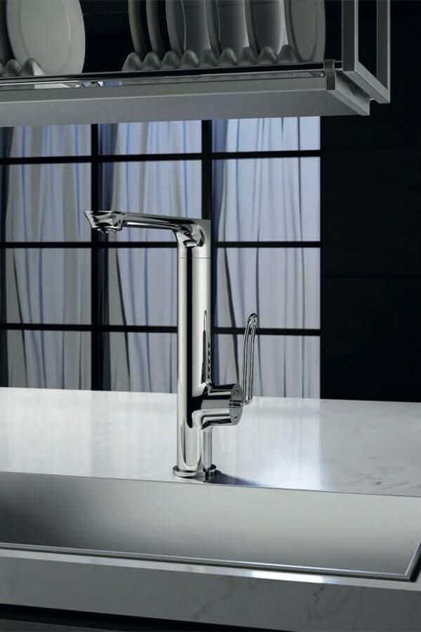 Grifo de cocina cromado sobre una encimera blanca, con un fondo de ventana oscura y un escurridor de platos encima.