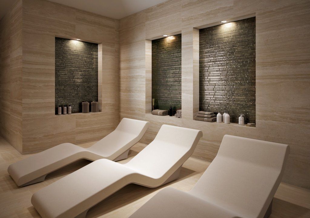 Salón spa con tres tumbonas blancas y nichos de piedra con productos.