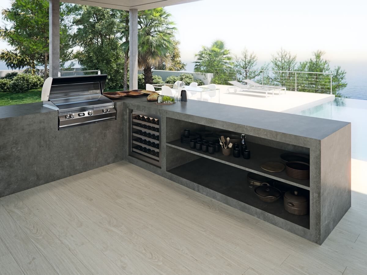 Cocina al aire libre con parrilla incorporada, refrigerador para vinos, estanterías y encimera, con vista a la piscina y al mar.