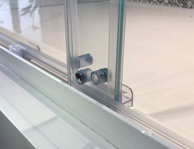 Puerta de ducha corrediza de vidrio sobre marco blanco, con dos mecanismos de rodadura transparentes.