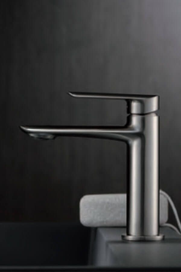 Grifo de baño de metal cepillado con un diseño moderno sobre un fondo oscuro.