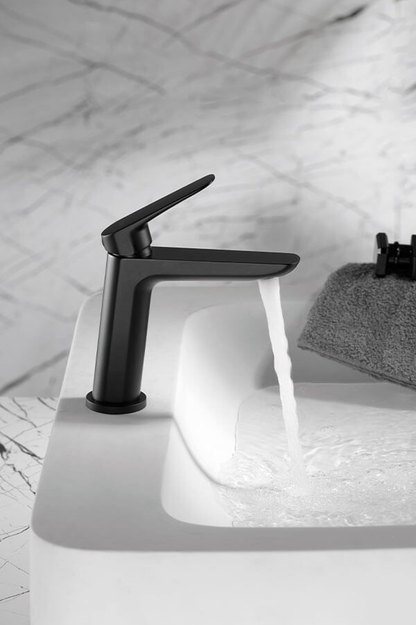 Grifo negro con agua corriente sobre lavabo blanco en baño.
