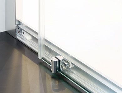 Primer plano de un mecanismo de puerta de ducha corrediza de vidrio en un riel de metal.