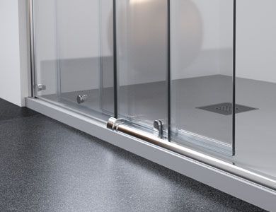 Puerta de ducha corrediza de vidrio con herrajes metálicos sobre base de ducha gris y piso oscuro.