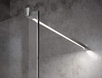 Una ducha con panel de vidrio, iluminada por una barra de luz LED horizontal montada en una pared gris texturizada.