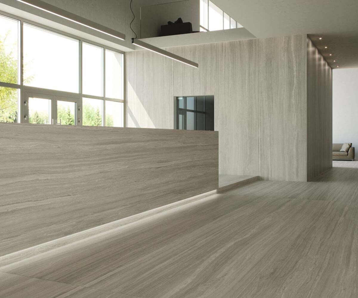 Área de recepción con paredes, mostrador y suelo de madera clara. Grandes ventanales, iluminación lineal y paleta de colores neutros.