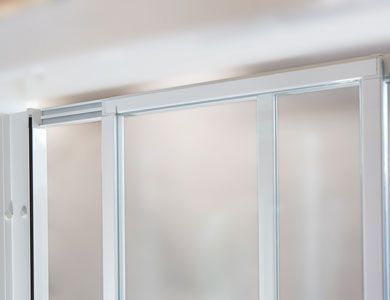 Puertas corredizas de vidrio con marco blanco instaladas sobre rieles de techo. Los paneles de vidrio esmerilado son visibles.