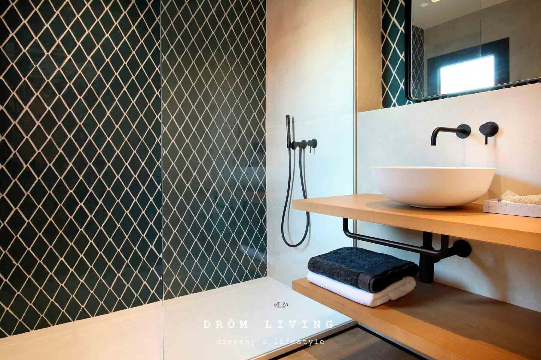 Baño moderno con ducha con azulejos de diamante verde oscuro, estante flotante de madera y lavabo blanco.