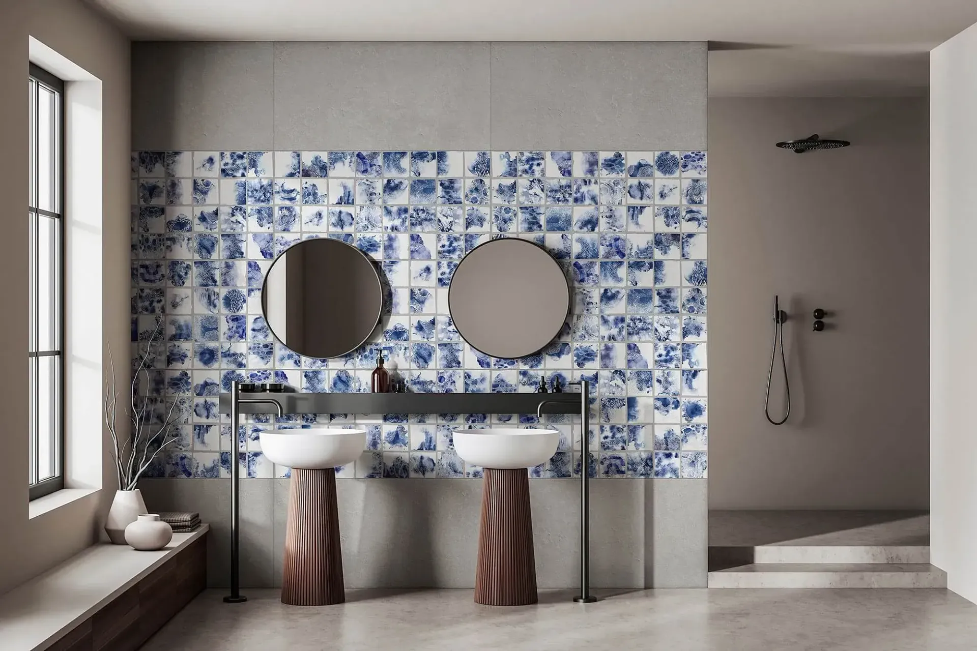 Baño con pared de azulejos azules y blancos, dos espejos redondos y dos lavabos de pedestal.