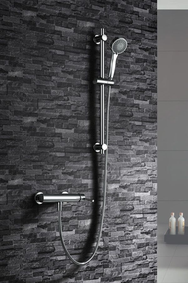 Accesorio de ducha cromado sobre una pared texturizada de color gris oscuro.