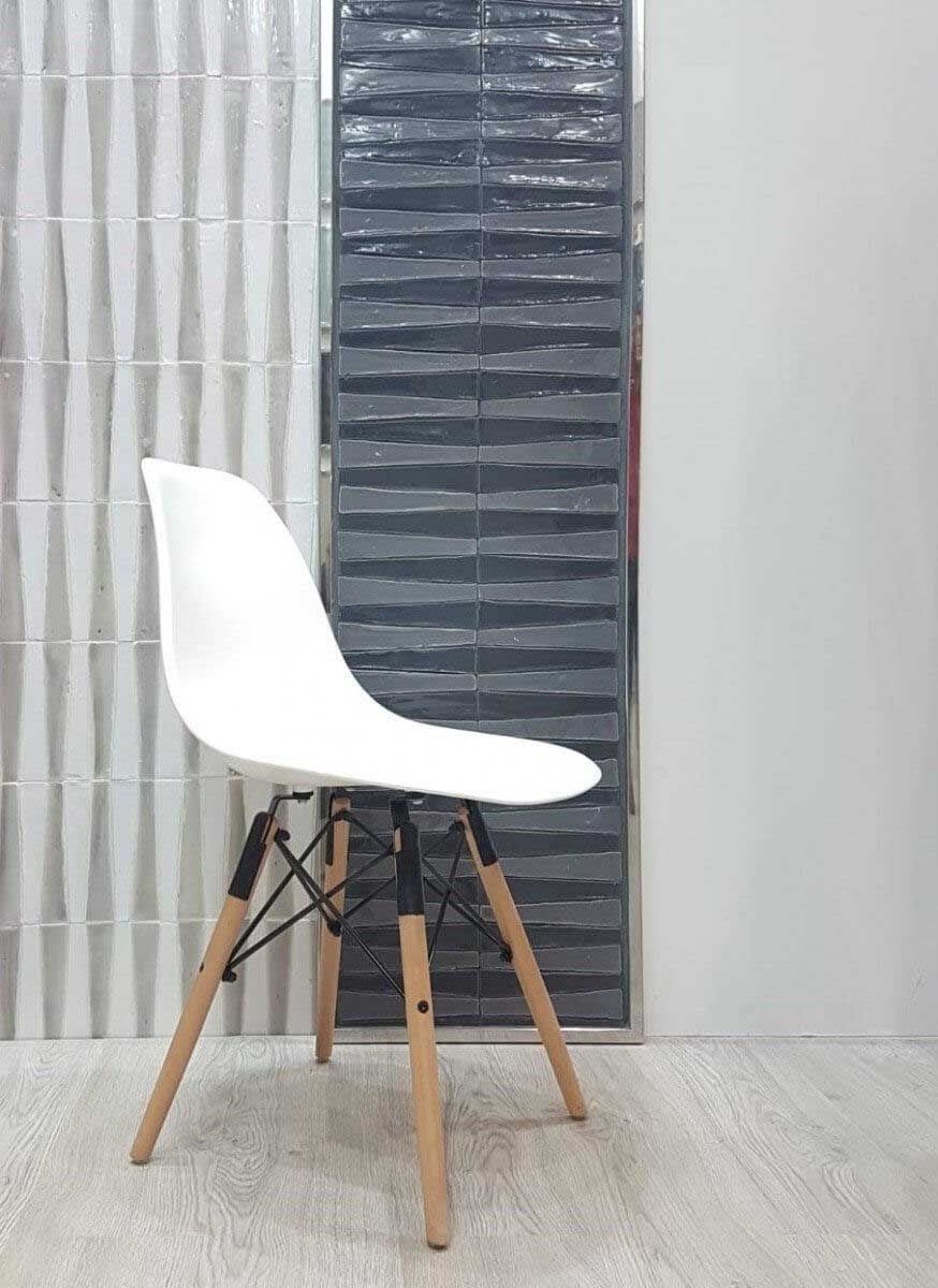 Silla blanca con patas de madera frente a azulejos de pared texturizados en gris y blanco.
