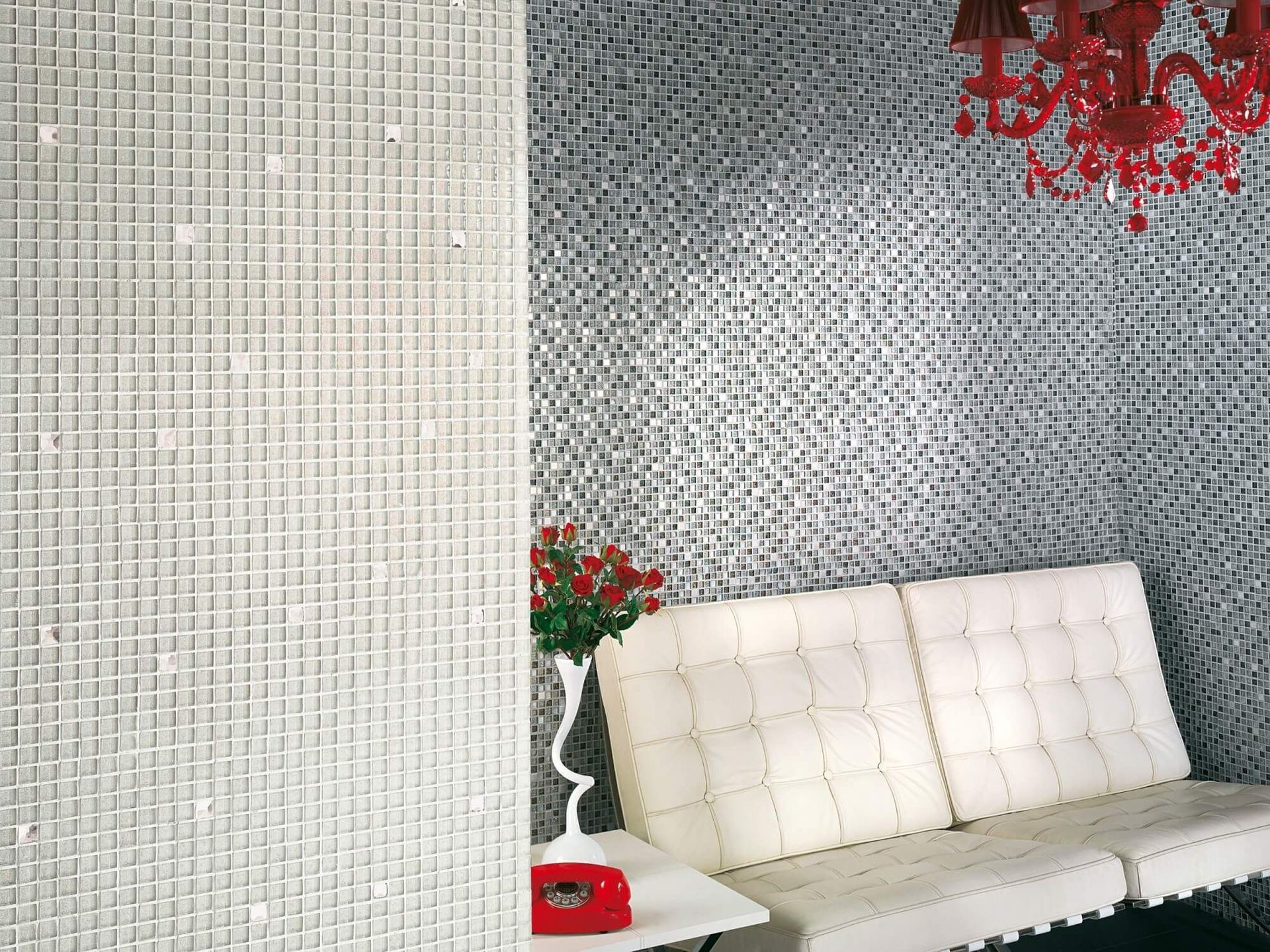 Pared de azulejos blancos y pared plateada estampada, un sofá blanco, una lámpara de araña roja y flores.