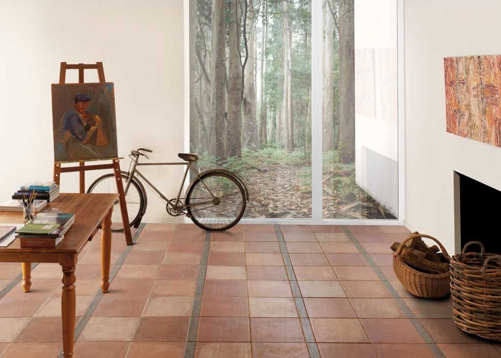 Habitación con suelo de baldosas, caballete, bicicleta, ventana con vistas a un bosque y una chimenea con cestas de leña.