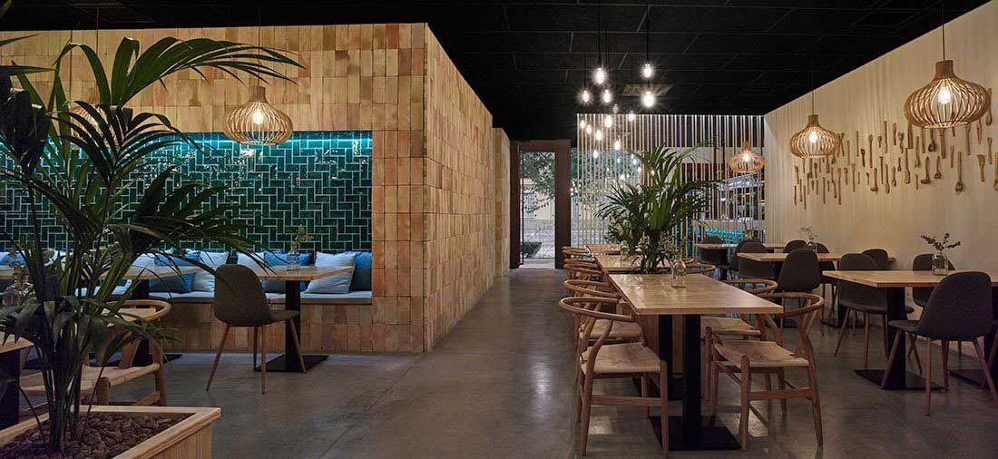 Vista interior de un restaurante moderno con paredes de madera, mesas y sillas, y una planta.