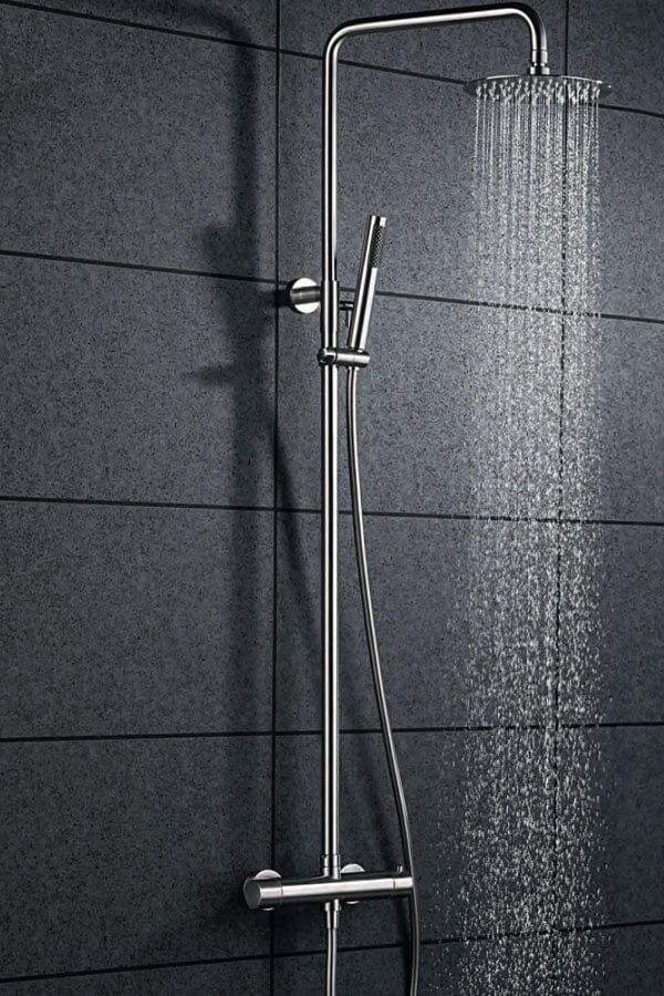 Cabezal de ducha plateado con agua cayendo sobre una pared de azulejos oscuros.