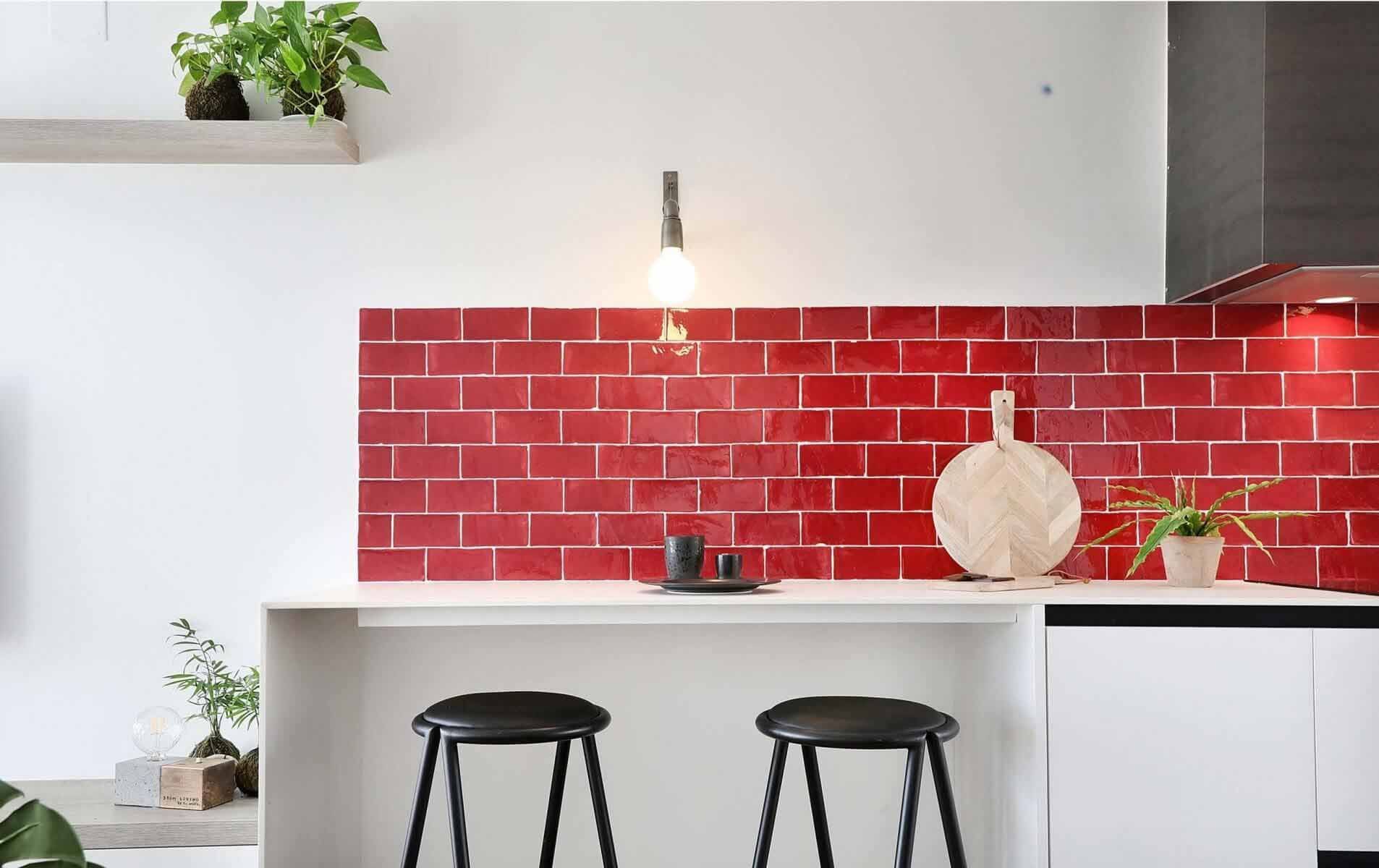 Salpicadero de cocina con azulejos rojos, encimera blanca y dos taburetes negros.