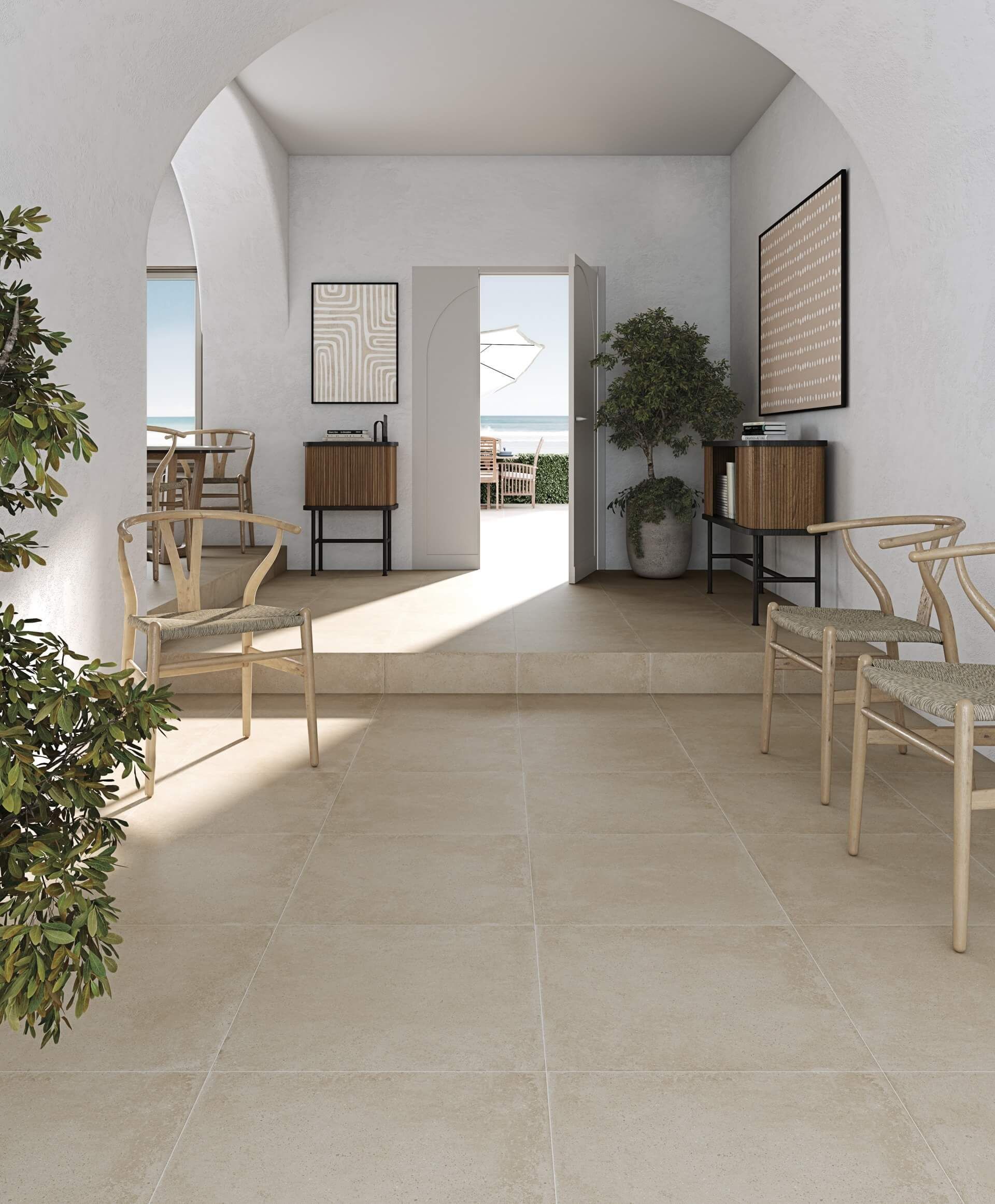Pasillo luminoso y arqueado con pisos de piedra, sillas y obras de arte que conduce a una vista exterior del océano.