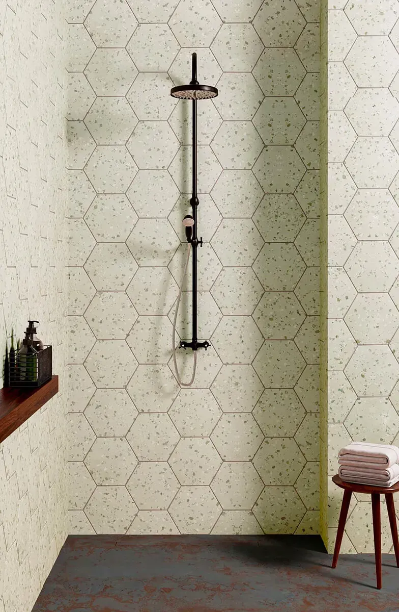 Ducha con grifería negra y paredes de azulejos moteados con diseño hexagonal. Suelo marrón, pequeña estantería de madera y taburete.