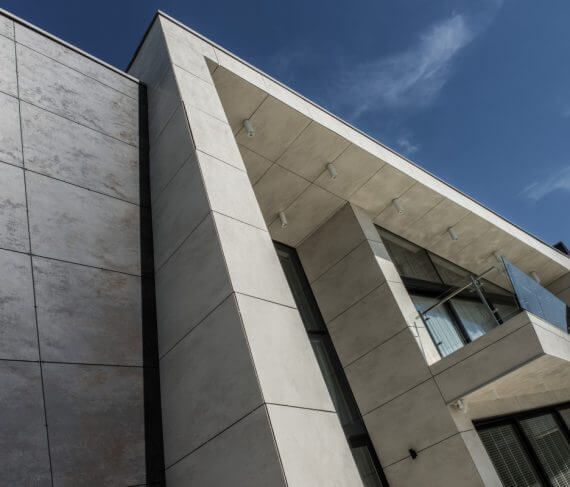 Edificio moderno con fachada de hormigón, arquitectura angular, ventanas de vidrio y cielo azul.
