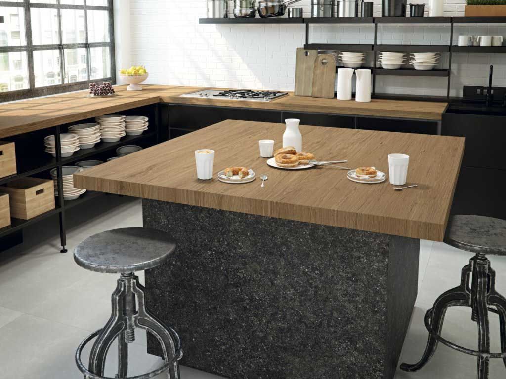 Cocina moderna con encimera de madera e isla de piedra, con taburetes, comida y vajilla.