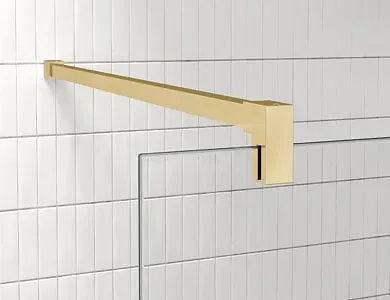 Brazo de ducha dorado instalado en una pared de azulejos blancos. El brazo es cuadrado, moderno y está fijado a la pared.