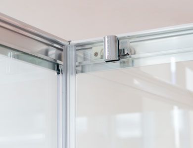 Primer plano de un mecanismo de puerta de ducha, que muestra un panel de vidrio corredizo y un riel de metal con rodillo.